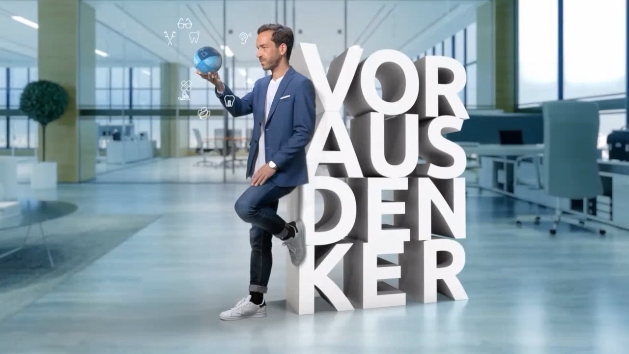 Man with a glowing sphere in a bright office, next to large white 3D letters “Vorausdenker”