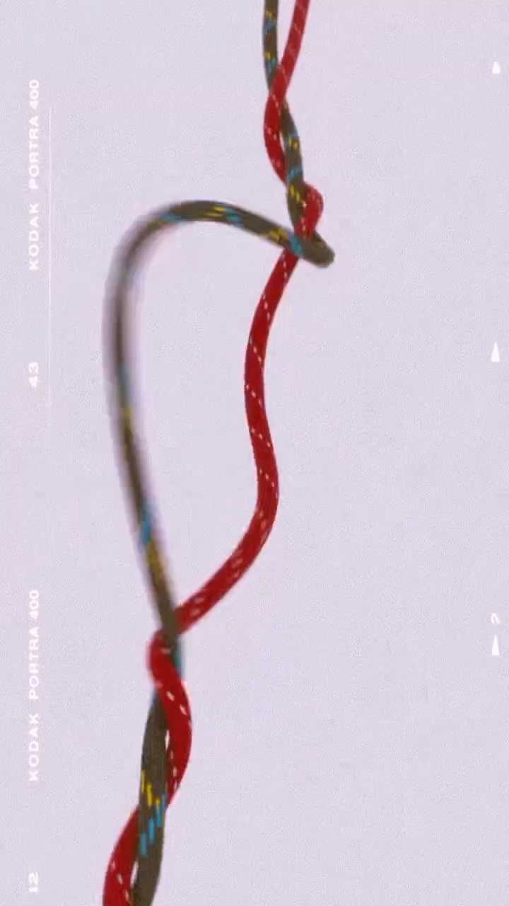 A red and a grey braided cord winding around each other against a light background, forming a loop